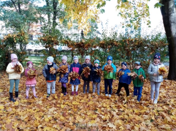 dzieci stoją w ogrodzi z bukietami liści
