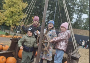 Dzieci pozują do zdjęcia na wozie z dyniami.