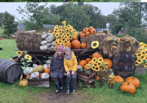 Dzieci pozują do zdjęcia przy wozie ozdobionym jesiennie.
