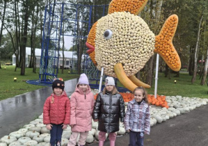 Dzieci stoja obok dekoracji jesiennej w kształcie ryby.