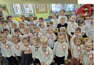 Dzieci ubrane na galowo śpiewają piosenkę.