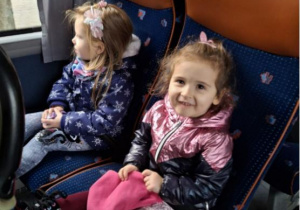 Dwie dziewczynki siedzą uśmiechnięte w autokarze.