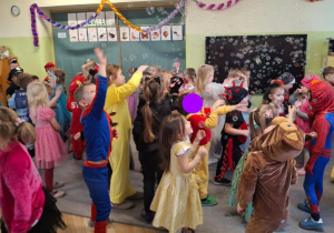 Dzieci w strojach karnawałowych tańczą na przystrojonej sali.
