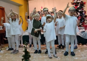 Dzieci w strojach aniołków śpiewają piosenkę.