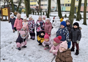 grupa dzieci pozuje z bałwanem w ogrodzie pełnym śniegu