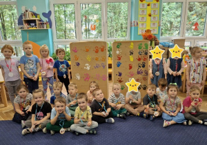 Dzieci siedzą obok pracy plastycznej, na której odciskały swoje dłonie
