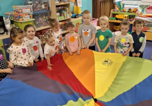 Dzieci bawią się chustą animacyjną stojąc wokół niej i trzymając ją za uchwyty