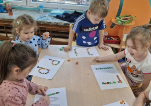 Dzieci przyklejają kropki na pracy plastycznej