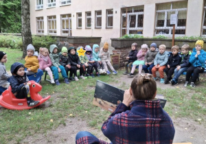 dzieci słuchają bajki czytanej przez nauczycielkę w ogrodzie przedszkolnym